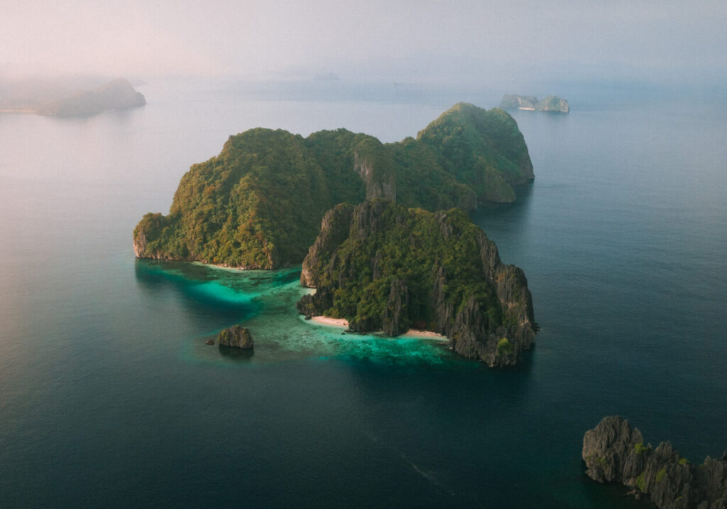 A lone island lined with limestone cliffs stands majestically amid the deep blue waters of Bacuit Bay.